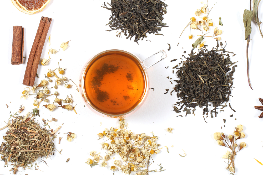 A cup of tea on a white table next to loose leaf teas